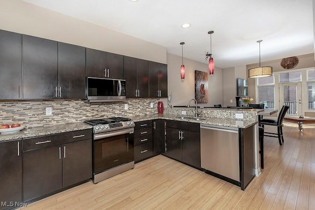 kitchen with light wood-type flooring, decorative backsplash, appliances with stainless steel finishes, a peninsula, and a sink