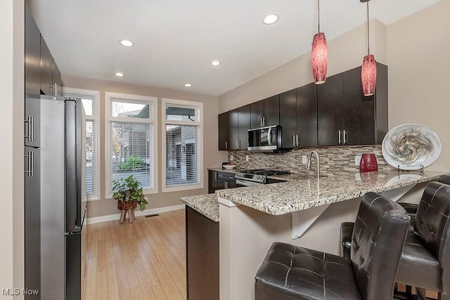 kitchen featuring light wood-type flooring, light stone counters, decorative backsplash, a peninsula, and stainless steel appliances