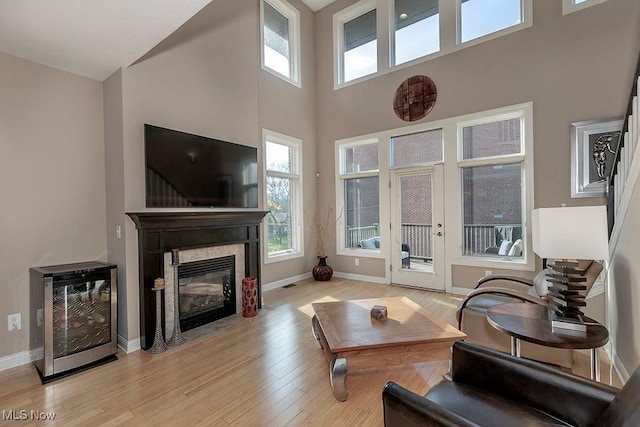 living area featuring baseboards, wine cooler, light wood-style floors, and a fireplace with flush hearth