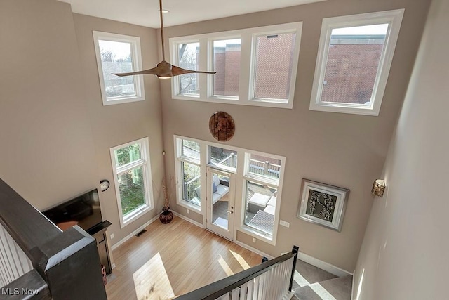 staircase with wood finished floors, visible vents, baseboards, a high ceiling, and ceiling fan