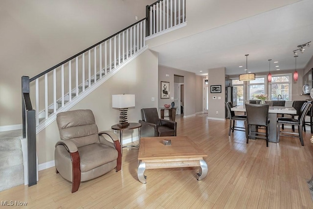 living room featuring stairs, light wood-type flooring, and baseboards