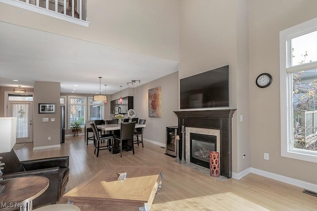 living area featuring a fireplace with flush hearth, plenty of natural light, light wood finished floors, and a towering ceiling