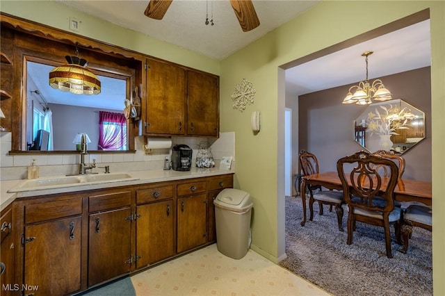 kitchen featuring light countertops, ceiling fan with notable chandelier, backsplash, and a sink