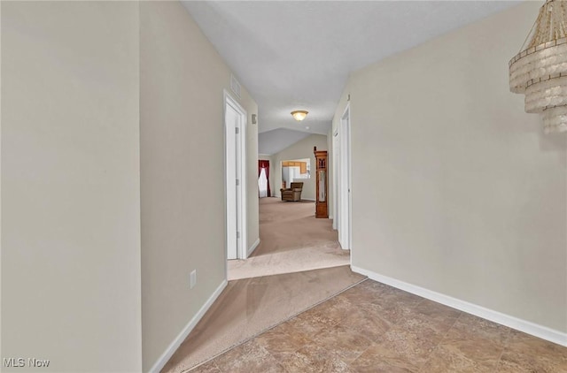 hallway featuring vaulted ceiling, carpet flooring, visible vents, and baseboards