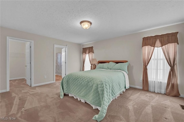 bedroom featuring a walk in closet, a textured ceiling, baseboards, and light carpet