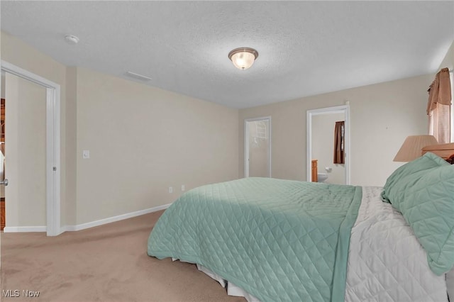 bedroom with visible vents, baseboards, light carpet, ensuite bath, and a textured ceiling