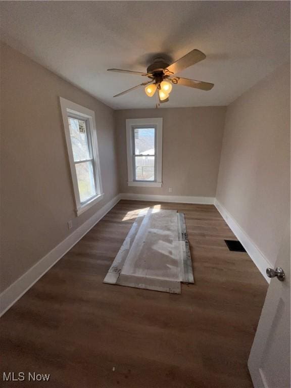 spare room with a ceiling fan, visible vents, wood finished floors, and baseboards