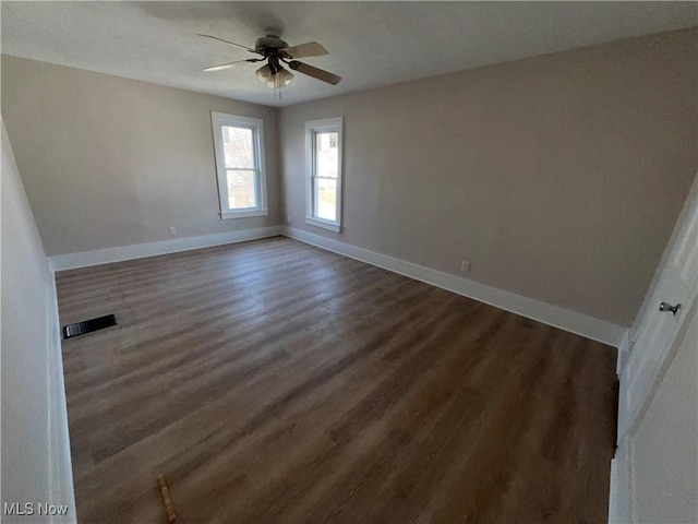 unfurnished room featuring visible vents, baseboards, dark wood-type flooring, and a ceiling fan