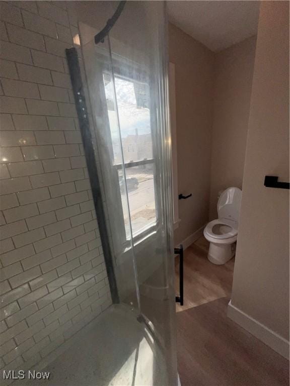 bathroom featuring a stall shower, toilet, baseboards, and wood finished floors