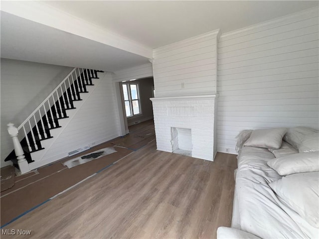 living room featuring stairway, a brick fireplace, wood finished floors, and ornamental molding