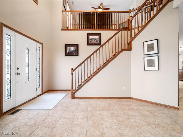 foyer entrance with light tile patterned flooring, stairs, baseboards, and a towering ceiling