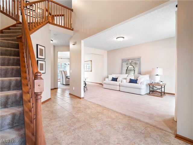 living room featuring a textured ceiling, a high ceiling, baseboards, light colored carpet, and stairs