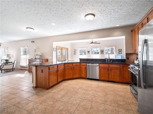 kitchen with a peninsula, a healthy amount of sunlight, brown cabinetry, and stainless steel appliances