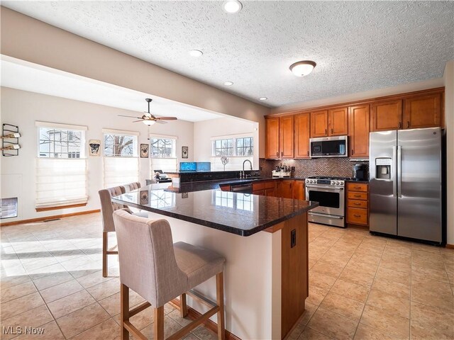 kitchen with a kitchen breakfast bar, tasteful backsplash, stainless steel appliances, a peninsula, and brown cabinetry