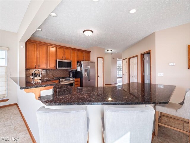 kitchen with a kitchen breakfast bar, backsplash, appliances with stainless steel finishes, and brown cabinetry