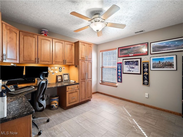 office space featuring visible vents, a textured ceiling, built in desk, baseboards, and ceiling fan