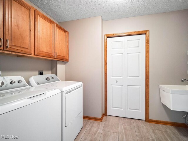 clothes washing area with a textured ceiling, cabinet space, independent washer and dryer, and baseboards