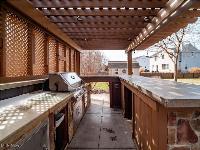 view of patio with an outdoor kitchen, a grill, a pergola, and fence