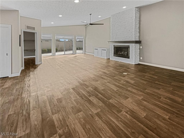 unfurnished living room with visible vents, a large fireplace, wood finished floors, a textured ceiling, and a ceiling fan