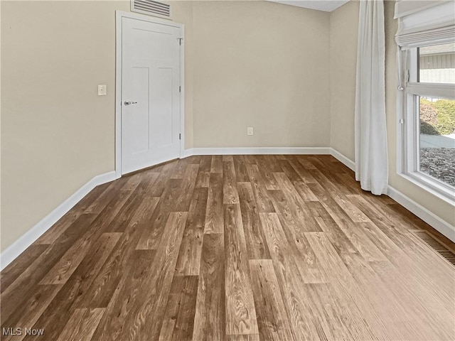 empty room with wood finished floors, visible vents, and baseboards