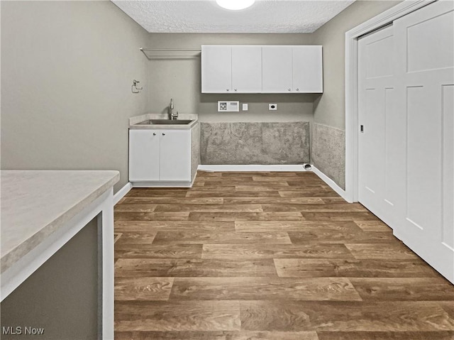 clothes washing area with a sink, baseboards, cabinet space, a textured ceiling, and dark wood-style flooring