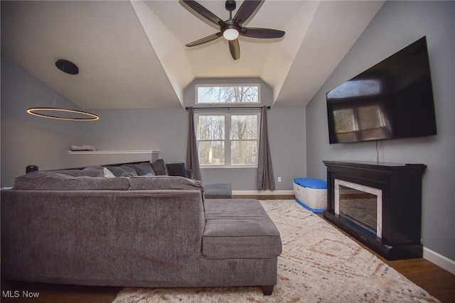 living room with a ceiling fan, wood finished floors, a fireplace, baseboards, and vaulted ceiling