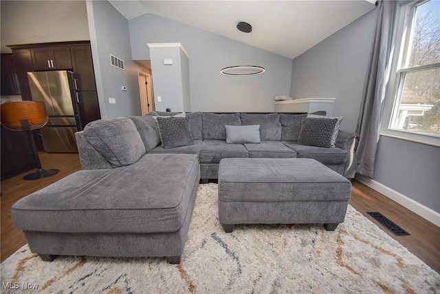 living area with visible vents, wood finished floors, baseboards, and vaulted ceiling