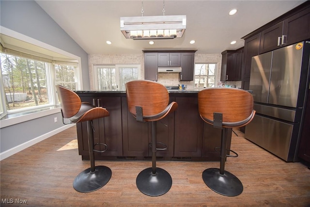 bar with light wood-type flooring, under cabinet range hood, freestanding refrigerator, recessed lighting, and lofted ceiling