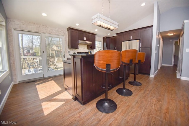 kitchen with visible vents, under cabinet range hood, light wood-type flooring, lofted ceiling, and fridge