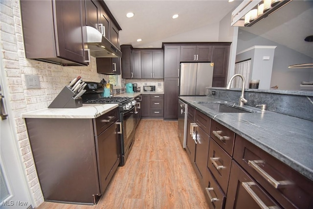 kitchen with dark brown cabinets, under cabinet range hood, lofted ceiling, appliances with stainless steel finishes, and a sink