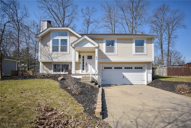 bi-level home featuring a front yard, fence, driveway, a chimney, and a garage