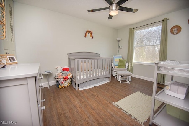 bedroom featuring baseboards, a crib, and wood finished floors