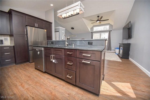 kitchen with light wood finished floors, a sink, lofted ceiling, appliances with stainless steel finishes, and a kitchen island with sink