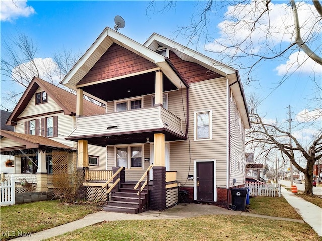 craftsman inspired home with a front lawn, a balcony, fence, and covered porch