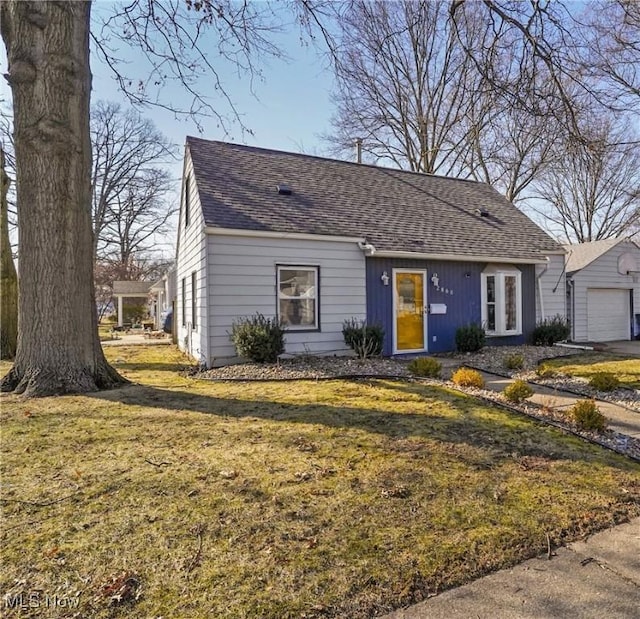 view of front of property featuring an outbuilding, a garage, a front lawn, and roof with shingles