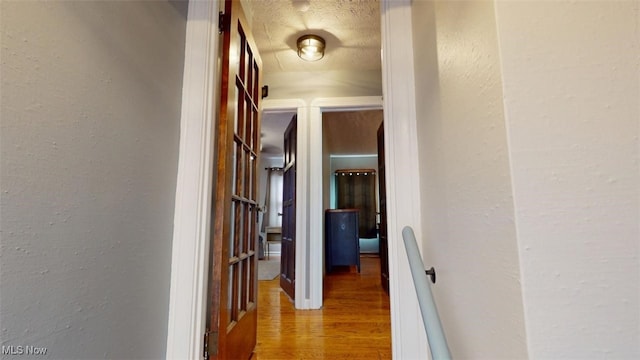 hallway with a textured ceiling, wood finished floors, and a textured wall