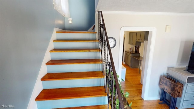 stairs with wood finished floors, baseboards, and ornamental molding