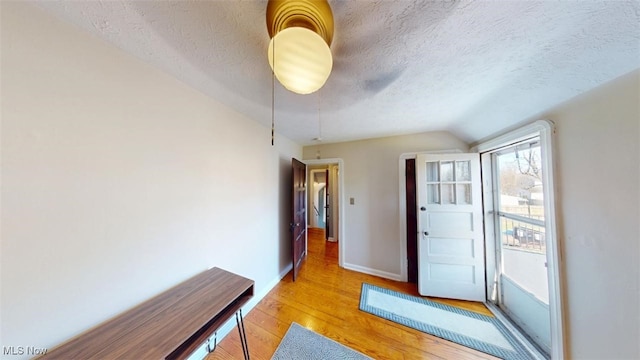 entrance foyer with baseboards, a textured ceiling, light wood-style flooring, and vaulted ceiling