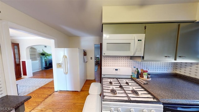 kitchen with light wood-type flooring, backsplash, dark countertops, white appliances, and arched walkways