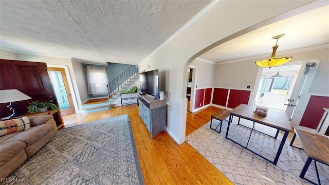 living room with arched walkways, light wood finished floors, a textured ceiling, and crown molding