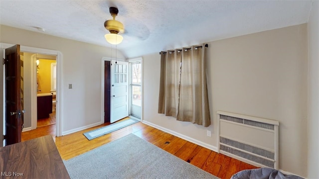 bedroom with radiator, wood finished floors, baseboards, ceiling fan, and a textured ceiling