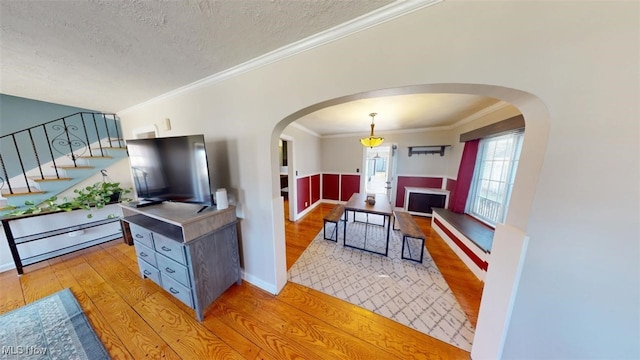 living room with stairway, light wood finished floors, arched walkways, ornamental molding, and a textured ceiling