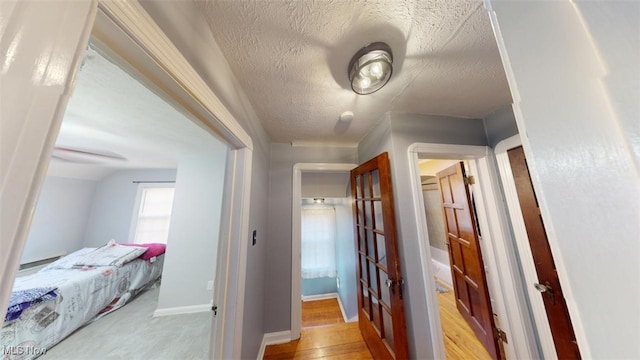 hall with baseboards, light wood-style floors, and a textured ceiling