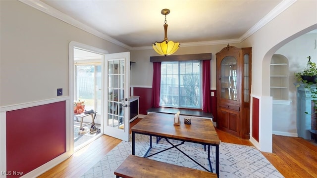 interior space featuring crown molding, built in shelves, arched walkways, and light wood-type flooring