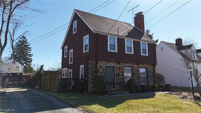 colonial-style house with stone siding, a front yard, a chimney, and fence