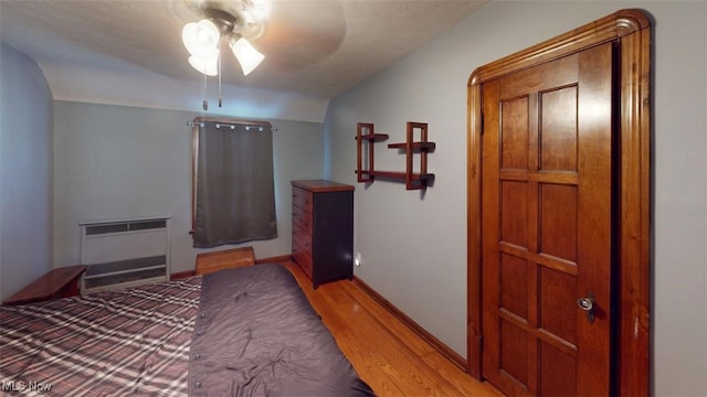 bedroom featuring a ceiling fan, radiator heating unit, light wood-style floors, and baseboards