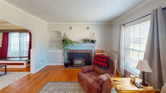 living room with crown molding, built in features, wood-type flooring, and a textured ceiling