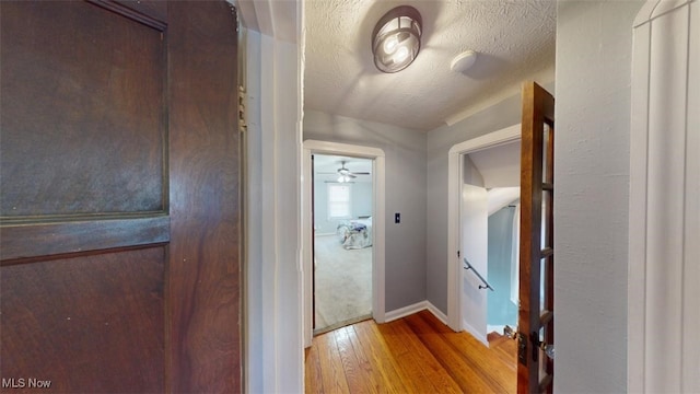 hallway featuring an upstairs landing, a textured ceiling, baseboards, and hardwood / wood-style flooring