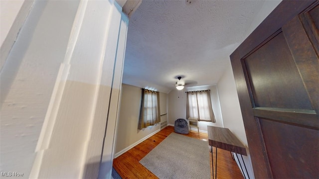 hallway featuring a textured ceiling, baseboards, and wood finished floors