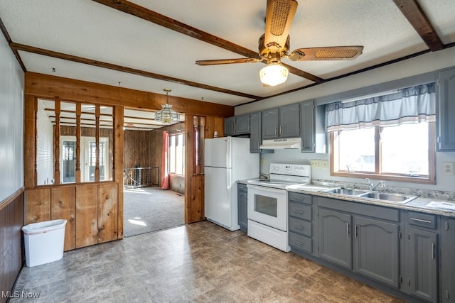 kitchen featuring gray cabinetry, a sink, under cabinet range hood, white appliances, and wooden walls